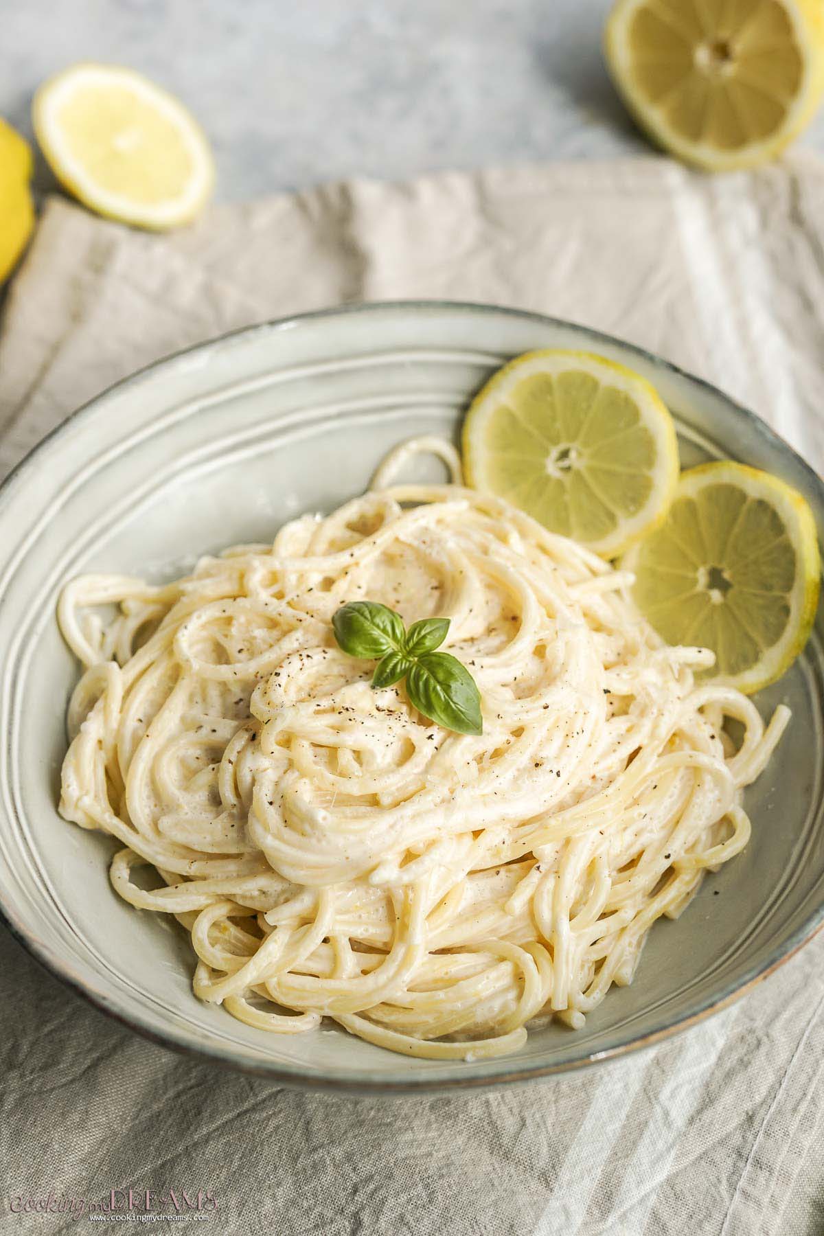creamy lemon spaghetti in a bowl with lemon slices and basil.